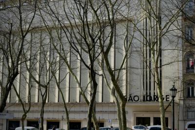 photograph “II.2020 — São Jorge” par David Farreny — www.farreny.net — Portugal, Lisbonne, Lisboa, Lisbon, ville, city, capitale, capital, bâtiment, immeuble, building, façade, facade, São Jorge, Saint-Georges, saint George, arbres, trees, platanes, plane trees, branches, lampadaire, street lamp, voitures, cars, passant, passer-by, piéton, pedestrian, panneau, sign, enseigne, fenêtres, windows