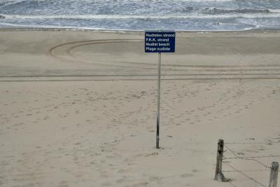 photograph “VI.2018 — Naked beach” par David Farreny — www.farreny.net — Pays-Bas, Netherlands, Nederland, Hollande, Holland, Hollande-Septentrionale, Zandvoort, mer du Nord, North sea, plage, beach, sable, sand, rivage, seashore, mer, sea, eau, water, poteau, post, pole, métal, metal, traces de pas, footprints, traces, vagues, waves, écume, foam, panneau, sign, Nudisten strand, F.K.K. strand, Nudist beach, Plage nudiste, clôture, fence, barbelés, barbed wires, bois, wood