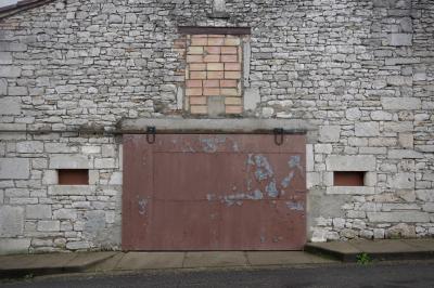 photograph “I.2024 — Closedown” par David Farreny — www.farreny.net — France, Occitanie, Tarn-et-Garonne, Septfonds, hanger, shed, entrepôt, warehouse, pierre, stone, mur, wall, portail, gate, métal, metal, fenêtre, window, parpaings, breeze-blocks, rue, street, trottoir, pavement, asphalte, asphalt, bitume, blacktop, fermé, closed down