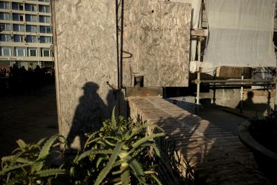 photograph “I.2019” par David Farreny — www.farreny.net — Italie, Italia, Italy, Campanie, Campania, Naples, Napoli, port, harbour, harbor, chantier, works, palissade, fence, échafaudage, scaffolding, muret, low wall, brique, brick, bois, wood, métal, metal, passants, passers-by, piétons, pedestrians, ombres, shadows, bâche, tarpaulin, sheet, immeuble, bâtiment, building, hôtel, hotel, enseigne, sign, fenêtres, windows, plantes, plants, Continental Hotel, hiver, winter, profusion, couple