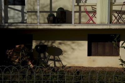 photograph “II.2015 — Faces of home, 98. Five minutes in the sun” par David Farreny — www.farreny.net — France, Occitanie, Aveyron, Rouergue, Ceignac, hiver, winter, maison, house, balcon, balcony, veranda, verandah, chaises, chairs, table, verre, glass, vitre, window, baie, barbecue, fenêtre, porte, door, grillage, fencing, clôture, fence, béton, concrete, métal, metal, jardin, garden, sous-sol, basement, volets, shutters, plantes, plants, pots, ombres, shadows