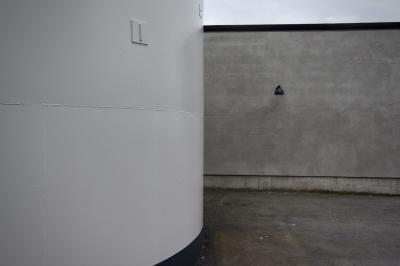 photograph “VI.2019 — Run away to the North, 173” par David Farreny — www.farreny.net — Norvège, Norway, Norge, Hordaland, Austevoll, Bekkjarvik, mur, wall, béton, concrete, gris, grey, paroi, lampe, lamp, noir, black, bitume, blacktop, asphalte, asphalt, citerne, cuve, tank, métal, metal, blanc, white, coin, corner, vide, empty, emptiness, parpaings, breeze-blocks