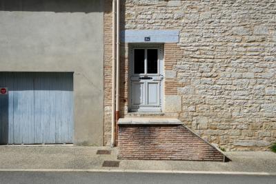 photograph “IV.2024 — Faces of home, 211” par David Farreny — www.farreny.net — France, Occitanie, Tarn-et-Garonne, Caussade, rue, street, ville, city, trottoir, pavement, asphalte, asphalt, bitume, blacktop, garage, portail, gate, bois, wood, pierre, stone, ciment, cement, gouttières, drainpipes, métal, metal, seuil, threshold, porte, door, plaque, plate, numéro, number, 8A, brique, brick, panneau, sign, interdiction de stationner, no parking