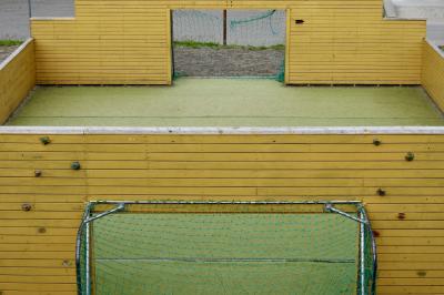 photograph “VII.2017 — Run away to the North, 116” par David Farreny — www.farreny.net — Norvège, Norway, Norge, Nord-Norge, Norvège du Nord, Troms, Harstad, sport, football, handball, pitch, ground, palissades, boarding, planches, planks, bois, wood, jaune, yellow, cages, buts, goals, filet, net, mur d'escalade, climbing wall, équipement, facility, métal, metal