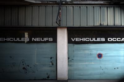 photograph “XII.2009” par David Farreny — www.farreny.net — France, Occitanie, Aveyron, Rouergue, Rodez, garage, fermé, closed down, vieux, old, vitrine, window, verre, vitre, glass, blanc d'Espagne, Spanish white, peinture, paint, enseigne, sign, tordue, twisted, véhicules neufs, véhicules d'occasion, métal, metal, reflet, reflection, graffitis