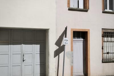photograph “IX.2024 — Faces of home, 229” par David Farreny — www.farreny.net — France, Occitanie, Tarn-et-Garonne, Montauban, maison, house, porte, door, fenêtres, windows, portail, gate, garage, panneau, sign, routier, roadsign, triangle, stop 30 m, grille, railings, métal, metal, volets, shutters, bois, wood, poignée, handle, ombre, shadow
