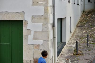 photograph “VII.2019 — Whatever” par David Farreny — www.farreny.net — Espagne, Spain, España, Navarre, Navarra, Pampelune, Pamplona, Bera, Vera, Vera de Bidasoa, pays Basque, ville, city, bourgade, town, rue, street, summer, été, bâtiment, building, pierre, stone, angle, coin, corner, portail, gate, bois, wood, vert, green, gouttière, drainpipe, métal, poteaux, posts, fenêtres, windows, verre, vitre, glass, trottoir, pavement, feuilles, mortes, dead, leaves, femme, woman, passante, passer-by, piétonne, pedestrian, bleu, blue, fatigue, tiredness