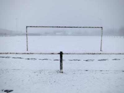 photograph “II.2013 — Melted snow” par David Farreny — www.farreny.net — France, Occitanie, Rouergue, Aveyron, Olemps, hiver, winter, terrain, football, field, plat, flat, but, goal, métal, metal, rouille, rust, rusty, brouillard, fog, froid, cold, ennui, boredom, poteaux, posts, poles, bâtiments, buildings, traces, pas, footprints, rectangle, dépression, depression