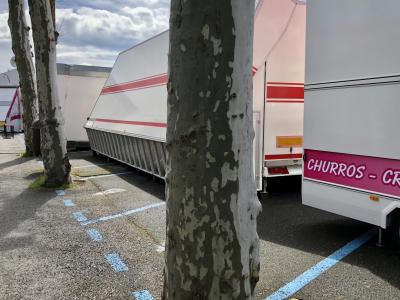 photograph “IV.2018 — Suspension of the party” par David Farreny — www.farreny.net — France, Occitanie, Gascogne, Gascony, Gers, Auch, fête foraine, funfair, fermée, closed, arbres, trees, platanes, plane trees, troncs, trunks, parking, car park, bitume, blacktop, asphalte, asphalt, peinture, paint, bleu, blue, camions, trucks, lorries, métal, metal, churros, nuages, clouds