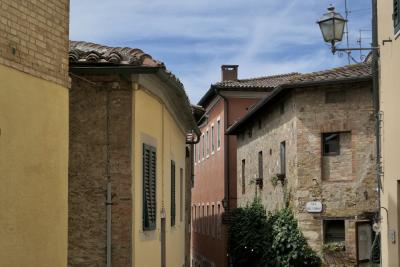 photograph “VIII.2022” par David Farreny — www.farreny.net — Italie, Italia, Italy, Toscane, Toscana, Tuscany, Sienne, Siena, San Quirico d'Orcia, rue, street, plaque, plate, via del Forno, maisons, houses, brique, brick, fenêtres, windows, volets, shutters, bois, wood, lampe, lamp, toits, roofs, tuiles, tiles, angles, coins, corners, cheminée, chimney, câbles, cables, fils, wires, gouttières, gutters, plantes, plants, antennes, antennas, ciel, sky