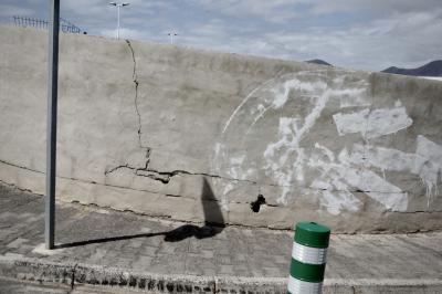 photograph “V.2016 — Lancerotte, 76” par David Farreny — www.farreny.net — Espagne, Spain, España, Canaries, Canarias, Lanzarote, Lancerotte, île, island, Playa Blanca, mur, wall, béton, concrete, trottoir, pavement, peinture, paint, poteau, post, pole, métal, metal, plastique, plastic, lampadaires, lamps, montagnes, mountains, ombre, shadow, fissure, crack