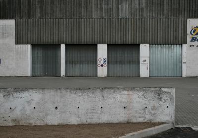 photograph “VI.2012” par David Farreny — www.farreny.net — France, industrie, industry, entrepôt, warehouse, béton, concrete, métal, metal, tôle ondulée, corrugated iron, portes, doors, portails, gates, lignes, lines, striures, stries, ridges, grooves, parallèles, parallels, gris, grey, gray, enseigne, sign, panneaux, roadsigns, muret, low wall, trous, holes, façade, facade, bâtiment, building, Occitanie, Aveyron, Rouergue, Onet-le-Château