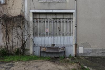 photograph “I.2024 — Faces of home, 208” par David Farreny — www.farreny.net — France, Occitanie, Tarn-et-Garonne, Septfonds, maison, house, bâtiment, immeuble, building, garage, portail, gate, métal, metal, fermé, closed, condamné, boarded up, tôle ondulée, corrugated iron, gouttière, drainpipe, trottoir, pavement, bitume, blacktop, asphalte, asphalt, panneau, sign, interdiction de stationner, no parking, volet, shutter, bois, wood, pierre, stone, crépi, roughcast