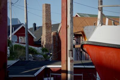 photograph “VII.2014 — Run away to the North, 200” par David Farreny — www.farreny.net — Norvège, Norge, Norway, Norvège du Nord, Nordland, Lofoten, Vågan, Henningsvær, port, harbour, bateau, boat, navire, ship, harbor, métal, metal, poteaux, posts, poles, bois, wood, maisons, houses, toits, roofs, tôle ondulée, corrugated iron, planches, planks, cheminée, chimney, briques, bricks, câbles, cables, fils, wires, barrière, fence, fenêtre, window, proue, bow, rochers, rocks, montagne, mountain, profusion