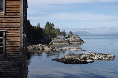 photograph “VI.2019 — Run away to the North, 178” par David Farreny — www.farreny.net — Norvège, Norge, Norway, Hordaland, Vestland, Austevoll, Huftarøy, Storebø, île, island, entrepôt, warehouse, bâtiment, immeuble, building, bois, wood, rive, shore, rivage, seashore, mer, sea, rochers, rocks, eau, water, arbres, trees, planches, planks, lampe, lamp, fenêtres, windows, montagnes, mountains, paysage, landscape, archipel, archipelago, Bratten