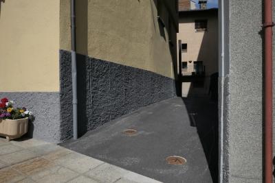 photograph “IX.2021” par David Farreny — www.farreny.net — Andorre, Andorra, Canillo, rue, street, ruelle, alley, bâtiments, buildings, immeubles, maison, house, bitume, blacktop, asphalte, asphalt, dallage, paving, tuyau, pipe, gouttière, drainpipe, métal, metal, coins, corners, angles, jardinière, planter, fleurs, flowers, béton, concrete, fenêtres, windows, ombre, shadow, balcon, balcony, cheminée, chimney