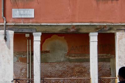 photograph “V.2022” par David Farreny — www.farreny.net — Italie, Italia, Italy, Vénétie, Veneto, Venise, Venice, Venezia, Venexia, San Trovaso, mur, wall, façade, facade, piliers, pillars, plaque, plate, Rio de S. Trovaso, gouttière, drainpipe, métal, metal, pierre, stone, bois, wood, brique, brick, rambarde, guardrail, câbles, cables, fils, wires, touriste, tourist, tête, head, tag, antifa, bêtise, dumbness, extrémisme, extremism, rouge, red, Dorsoduro