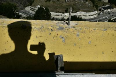 photograph “VIII.2023 — Headache facing the world” par David Farreny — www.farreny.net — Andorre, Andorra, Canillo, route, road, bitume, blacktop, asphalte, asphalt, béton, concrete, barrière, barrier, jaune, yellow, barre, métal, metal, bar, rambarde, guardrail, ombre, shadow, tête, head, main, hand, épaules, shoulders, photographe, photographer, autoportrait, selfportrait, fatigue, usure, wear, colline, hill, contrebas, below, voitures, cars, circulation, trafic, traffic, bâtiment, building, garage, arbres, trees