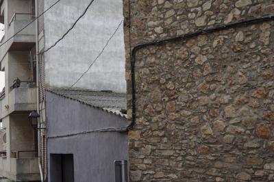 photograph “XI.2021 — Faces of home, 130” par David Farreny — www.farreny.net — Espagne, España, Spain, Catalogne, Cataluña, Catalunya, Catalonia, Lérida, Lleida, Alt Urgell, Coll de Nargó, bourgade, town, village, rue, street, bâtiments, buildings, immeuble, mur, wall, pierre, stone, câbles, cables, fils, wires, garage, portail, gate, béton, concrete, toit, roof, tôle ondulée, corrugated iron, panneau, sign, balcons, balconies, gouttière, drainpipe, lampe, lamp, domicile, home