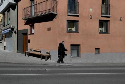 photograph “II.2023” par David Farreny — www.farreny.net — Andorre, Andorra, Canillo, rue, street, bitume, blacktop, asphalte, asphalt, trottoir, pavement, bâtiment, immeuble, building, fenêtres, windows, balcon, balcony, angle, coin, corner, banc, bench, porte, door, rideau, métal, metal, curtain, magasin, store, shop, passante, passer-by, piétonne, pedestrian, femme, woman, vieille, old, fleurs, flowers, ombre, shadow, verre, vitre, glass