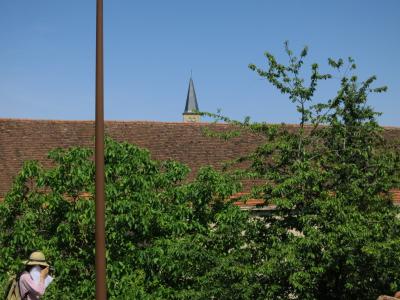 photograph “VI.2012” par David Farreny — www.farreny.net — France, village, toit, roof, toiture, roofing, tuiles, tiles, arbres, trees, lampadaire, réverbère, street lamp, métal, metal, clocher, steeple, tower, église, church, femme, woman, photographe, photographer, été, summer, chapeau, paille, straw, hat, sac à dos, backpack, rucksack, Occitanie, Rouergue, Aveyron, Naussac, É*