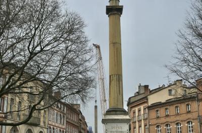 photograph “III.2024” par David Farreny — www.farreny.net — France, Occitanie, Haute-Garonne, Toulouse, ville, city, place, square, bâtiments, buildings, brique, brick, place Dupuy, monument, inscription, À Dupuy et aux braves, colonne, column, 1834, fenêtres, windows, arbres, trees, branches, branchages, grue, crane, chaînes, chains, béton, concrete, travaux, works, métro, subway, underground, métal, metal, toits, roofs