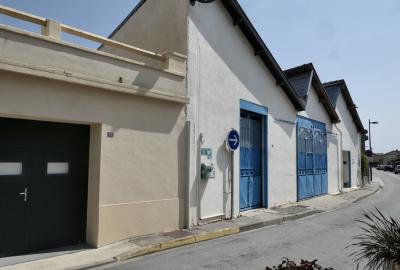 photograph “VIII.2024” par David Farreny — www.farreny.net — France, Occitanie, Tarn-et-Garonne, Caussade, ville, city, bourgade, town, atelier, workshop, usine, factory, porte, door, portails, gates, métal, metal, rue, street, trottoir, pavement, bitume, blacktop, asphalte, asphalt, panneau, sign, flèche, arrow, droite, right, toit, roof, dents de scie, sawtooth, shed, terrasse, terrace, lampadaire, lamp, voitures, cars, industrie, industry, plaque, plate, numéro, number, 13, plantes, plants