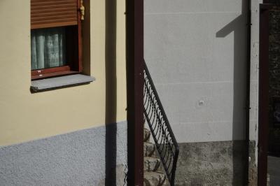 photograph “II.2023 — Faces of home, 172” par David Farreny — www.farreny.net — Andorre, Andorra, Canillo, maison, house, mur, wall, fenêtres, windows, stores, rideau, curtain, crépi, roughcast, ciment, cement, béton, concrete, escalier, staircase, stairs, marches, steps, rambarde, guardrail, rampe, railing, métal, metal, poteau, post, pole, ombre, shadow, domicile, home