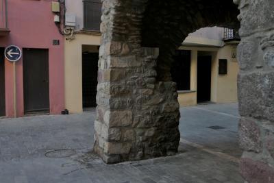 photograph “I.2023 — Elephant” par David Farreny — www.farreny.net — Espagne, España, Espanya, Spain, Catalogne, Cataluña, Catalunya, Lleida, Lérida, Alt Urgell, La Seu d'Urgell, ville, city, rue, street, maisons, houses, pilier, pillar, pierre, stone, patte, paw, éléphant, elephant, panneau, routier, sign, roadsign, flèche, arrow, gauche, left, portes, doors, fenêtres, windows, balcon, balcony, coin, corner, angle, câbles, cables, fils, wires, plaque, plate, numéro, number, 84, dallage, paving