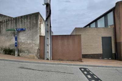 photograph “I.2022 — Whatever” par David Farreny — www.farreny.net — Espagne, España, Espanya, Spain, Catalogne, Cataluña, Catalunya, Comarques gironines, Gérone, Gerona, Girona, Alto Ampurdán, Alt Empordà, Pau, rue, street, murs, walls, bitume, blacktop, asphalte, asphalt, panneaux, signs, métal, metal, hiver, winter, bâtiments, buildings, trottoir, pavement, côte, slope, poteau, post, pole, câbles, cables, fils, wires, brique, brick, ralentisseur, speed bump, porte, door, poignée, handle, boîte, box, baies, windows, nuages, clouds, caillou, stone