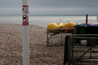 photograph “V.2013” par David Farreny — www.farreny.net — Royaume-Uni, United Kingdom, Grande-Bretagne, Great Britain, Angleterre, England, UK, GB, Sussex, West Sussex, Worthing, front de mer, seafront, plage, beach, galets, pebbles, shingle, mer, sea, Manche, Channel, horizon, eau, water, paysage, landscape, marin, seascape, poteau, post, pole, métal, metal, autocollant, sticker, interdit, forbidden, danger, chiens, dogs, offshore winds, bouées, buoys, yellow, jaune, portail, gate, clôture, fence, grillage, fencing, poubelles, trash, bins, cans, plastique, plastic, profusion