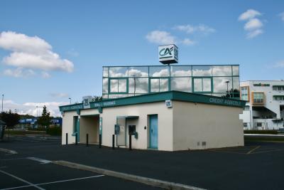 photograph “IX.2011 — Trade on Sunday” par David Farreny — www.farreny.net — France, Occitanie, Aveyron, Rouergue, Onet-le-Château, centre commercial, mall, parking, car park, bâtiments, immeubles, buildings, banque, bank, Crédit Agricole, bitume, blacktop, asphalte, asphalt, porte, door, baies, fenêtres, windows, verre, vitre, glass, reflet, reflection, nuages, clouds, ciel, sky, logo, distributeur, ATM, arbres, trees, laideur, ugliness, laid, ugly