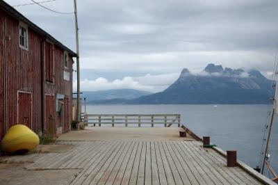 photograph “VII.2014 — Run away to the North, 134” par David Farreny — www.farreny.net — Norvège, Norway, Norge, Nordland, Norvège du Nord, Nord-Norge, Salten, Hamarøy, Tranøy, Tranøya, port, harbour, harbor, jetée, pier, bois, wood, bâtiment, building, entrepôt, warehouse, bateau, boat, montagne, mountain, Tilthornet, paysage, landscape, nuages, clouds, carte postale, eau, water, mer, sea, bouée, buoy, jaune, yellow, rambarde, guardrail, planches, planks, vue, view, abandonné, abandoned, câbles, cables, fils, wires, postcard