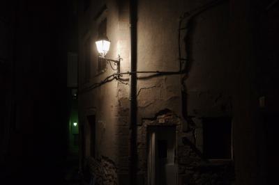 photograph “I.2024 — Faces of home, 207” par David Farreny — www.farreny.net — France, Occitanie, Tarn-et-Garonne, Saint-Antonin-Noble-Val, nuit, night, soir, evening, rue, street, village, town, bourgade, maison, house, lampadaires, lamps, pénombre, darkness, sombre, dark, porte, door, plaque, plate, numéro, number, 7, gouttière, drainpipe, fil, wire, câble, cable, pierre, stone, enduit, roughcast, métal, metal, fenêtres, windows, volets, shutters, bois, wood, domicile, home