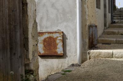 photograph “III.2021” par David Farreny — www.farreny.net — France, Aquitaine, Lot-et-Garonne, Nérac, ville, city, rue, street, coin, corner, angle, gouttière, drainpipe, ciment, cement, pierre, stone, marches, steps, escalier, stairs, staircase, planches, planks, bois, wood, pissenlit, dandelion, fleur, flower, plaque, plate, métal, metal, rouille, rust, rusty, symbole, symbol, maison, house, gaz, gas, GDF, charnières, hinges, panneau, routier, sign, roadsign, trottoir, pavement