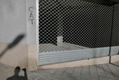 photograph “I.2023” par David Farreny — www.farreny.net — Espagne, España, Espanya, Spain, Catalogne, Cataluña, Catalunya, Lleida, Lérida, Alt Urgell, La Seu d'Urgell, ville, city, rue, street, angle, coin, corner, bâtiment, immeuble, building, béton, concrete, trottoir, pavement, pierre, stone, grille, fencing, métal, metal, rideau, curtain, bloc, block, ombre, shadow, lampadaire, lamp, autoportrait, selfportrait, photographe, photographer, graffiti, tag, CAT
