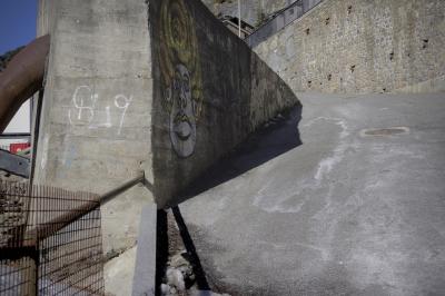photograph “II.2023” par David Farreny — www.farreny.net — Andorre, Andorra, Ordino, rue, street, path, voie, pente, slope, bit, bitume, blacktop, asphalte, asp, asphalt, paroi, wall, béton, concrete, pierre, stone, grillage, fencing, tuyau, pipe, métal, metal, rambarde, guardrail, tags, S19, visage, face, ombre, shadow, maisons, houses, rocher, rock