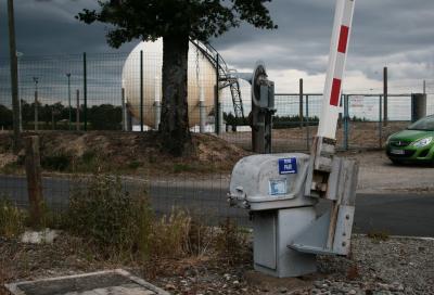 photograph “VII.2011 — Meeting point” par David Farreny — www.farreny.net — France, Occitanie, Aveyron, Rouergue, Ceignac, route, road, grillage, fence, fencing, voiture, verte, green, car, vert, passage à niveau, level crossing, grade crossing, inscription, sign, SENS PAIR →, barrière, gate, portail, arbre, tree, réservoir, reservoir, tank, gaz, gas, sphère, sphere, herbe, grass, végétation, vegetation, poteaux, posts, poles, cailloux, stones, ballast, roadbed, métal, metal, feu, light, profusion, industrie, industry