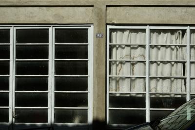 photograph “III.2025 — 86 ↻ 98” par David Farreny — www.farreny.net — France, Occitanie, Gascogne, Gascony, Lomagne, Gers, Fleurance, ville, city, bourgade, town, bâtiment, building, baies, windows, fenêtres, verre, vitre, glass, rectangles, rideau, curtain, vieux, old, traces, marks, plaque, plate, renversée, overturned, inversée, inverted, nombre, number, 98, 86, chiffres, numbers, digits, numéro, ciment, cement, béton, concrete, voiture, car, métal, metal, reflet, reflection, ombre, shadow, porte, door, poignée, handle