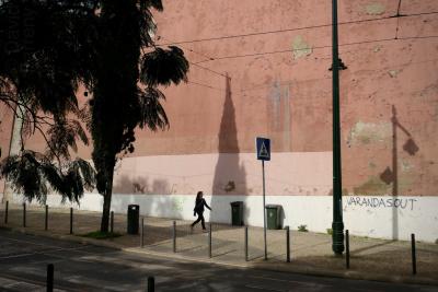 photograph “II.2020” par David Farreny — www.farreny.net — Portugal, Lisbonne, Lisboa, Lisbon, ville, city, capitale, capital, rue, street, mur, wall, arbre, tree, ombre, shadow, branches, cyprès, cypress, poteaux, posts, poles, métal, metal, câbles, cables, fils, wires, poubelles, bins, trash, cans, trottoir, pavement, pierre, stone, graffiti, Varandasout, panneau, routier, sign, roadsign, passante, passer-by, piétonne, pedestrian, femme, woman, jeune, young, bitume, blacktop, asphalte, asphalt