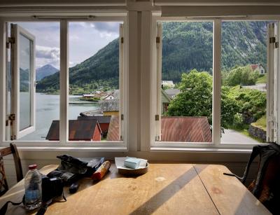 photograph “VI.2019 — Run away to the North, 301. Expired trip” par David Farreny — www.farreny.net — Norvège, Norway, Norge, Sogn og Fjordane, Sogndal, Fjærland, Mundal, maisons, houses, bois, wood, fenêtres, windows, vue, view, verre, vitre, glass, paysage, landscape, fjord, eau, water, toits, roofs, tôle ondulée, corrugated iron, ardoise, slate, métal, metal, table, ombre, shadow, arbres, trees, montagnes, mountains, nuages, clouds, rue, street, chaise, chair, sac à dos, backpack, appareil photo, camera, reflex, bouteille, bottle, plastique, plastic, batterie, battery, biscuits, papier, paper, feuilles, sheets, charnières, hinges, câble, cable, fil, wire, mur, wall, pierre, stone, quai, dock, bancs, benches, forêt, forest, carte postale, postcard