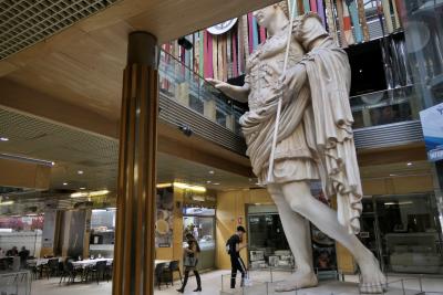 photograph “III.2023” par David Farreny — www.farreny.net — Espagne, España, Spain, Aragon, Aragón, Saragosse, Zaragoza, Caesaraugusta, centre commercial, mall, bâtiment, immeuble, building, intérieur, inside, statue, géant, giant, César, Caesar, Auguste, Augustus, rambarde, guardrail, verre, vitre, glass, bois, wood, pilier, pillar, colonne, column, magasins, shops, stores, restaurants, tables, chaises, chairs, passants, passers-by, piétons, pedestrians, jeune, young, homme, man, femme, woman, smartphones, art, empereur, emperor, romain, roman, Rome, antique, ancient, histoire, history, commerce, profusion, sculpture