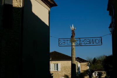 photograph “XII.2017” par David Farreny — www.farreny.net — village, maisons, houses, pierre, stone, hiver, winter, décembre, December, fêtes, festive season, statue, ange, angel, saint, Michel, Michael, archange, archangel, colonne, column, ailes, wings, enseigne, sign, bonnes fêtes, happy festive season, étoile, star, ombre, shadow, sombre, dark, pénombre, darkness, lampe, lamp, rue, street, fenêtre, window, volets, shutters, arbres, trees, christianisme, Christianism, religion, catholicisme, Catholicism, lettres, letters, caractères, characters, inversés, inverted, mirrored, vœux, greetings, fin d'année, end of year, France, Occitanie, Gascogne, Gers, Lavardens