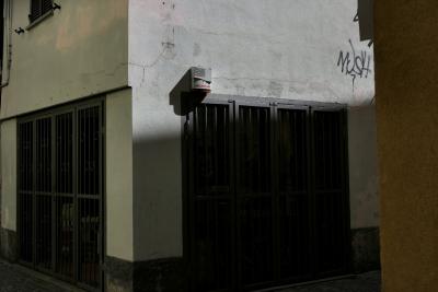 photograph “VII.2022 — Mush” par David Farreny — www.farreny.net — Italie, Italia, Italy, Ligurie, Liguria, Savone, Savona, Cairo Montenotte, Cairi, ville, city, rue, street, ruelle, alley, angle, coin, corner, portail, gate, grille, railings, tag, Mush, boîtier, box, appareil, device, alarme, alarm, mur, wall, ombre, shadow