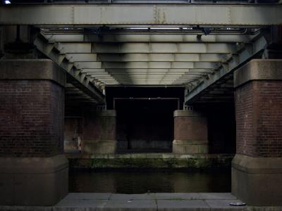 photograph “X.2017 — Blonde” par David Farreny — www.farreny.net — Pays-Bas, Netherlands, Nederland, Hollande, Holland, Amsterdam, pont, bridge, piliers, pillars, brique, brick, métal, metal, canal, poutres, beams, bank, berge, femme, woman, blonde, passante, passer-by, piétonne, pedestrian, pierre, stone