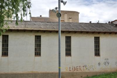 photograph “VI.2023 — Libert” par David Farreny — www.farreny.net — Espagne, España, Espanya, Spain, Catalogne, Cataluña, Catalunya, Catalonia, Lérida, Lleida, Solsonès, Solsona, ville, city, bâtiment, building, fenêtres, windows, tags, graffitis, LIBERT, laid, ugly, laideur, ugliness, mur, wall, béton, concrete, toit, roof, tôle ondulée, corrugated iron, herbe, grass, tuiles, tiles, cheminées, chimneys, lampadaire, lampes, lamps, poteau, post, pole, métal, metal, feuillage, foliage, ciel, sky, nuages, clouds