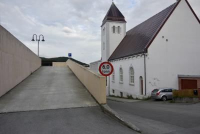 photograph “VII.2017 — Run away to the North, 243” par David Farreny — www.farreny.net — Norvège, Norway, Norge, Troms, Midtre Hålogland, Harstad, ville, city, église, church, parking, car park, béton, concrete, lampadaire, lamp, voiture, car, rue, street, bitume, blacktop, asphalte, asphalt, clocher, bell tower, panneau, routier, sign, roadsign, 60 tonn, toit, roof, nuages, clouds, rampe, ramp