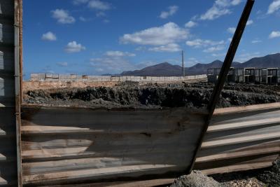 photograph “II.2018 — Lancerotte, 60” par David Farreny — www.farreny.net — Espagne, España, Spain, Canaries, Canarias, Canary, Lanzarote, Lancerotte, île, island, montagnes, mountains, volcans, volcanoes, chantier, building site, abandonné, abandoned, palissade, tôle ondulée, corrugated iron, métal, metal, clôture, fence, rouille, rust, rusty, béton, concrete, structure, pylône, électrique, electricity, pole, post, nuages, terre, sol, earth, soil, noir, black, trou, hole