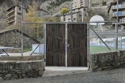 photograph “XI.2022 — Whatever” par David Farreny — www.farreny.net — Andorre, Andorra, Canillo, terrain, sport, field, grillage, clôture, fence, fencing, métal, metal, porte, door, rue, street, bitume, blacktop, asphalte, asphalt, muret, low wall, pierre, stone, maison, house, immeubles, bâtiments, buildings, balcons, balconies, fenêtres, windows, ville, city, bourgade, town, panier, basket, basketball, hoop, voiture, car, mountain, montagne