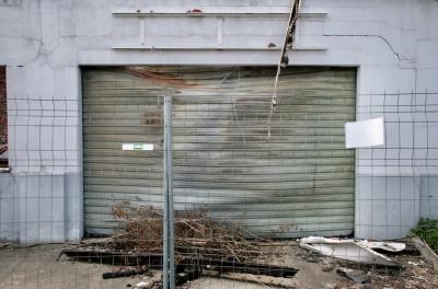 photograph “IV.2010” par David Farreny — www.farreny.net — France, Occitanie, Haute-Garonne, Villemur-sur-Tarn, garage, incendie, fire, feu, portail, gate, métal, metal, gondolé, warped, déformé, distorted, béton, concrete, barrière, barrier, clôture, fence, poutre, beam, carbonisée, charred, branches, branchages